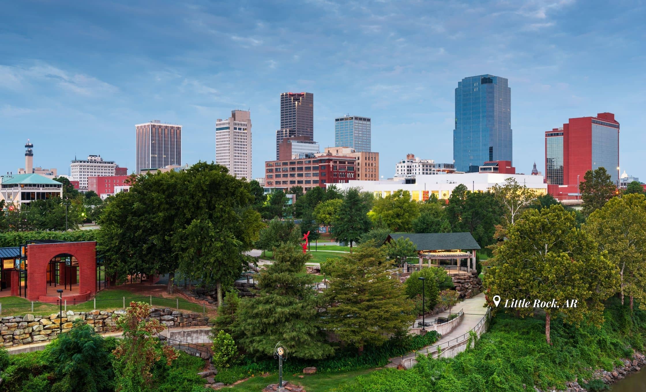 City skyline of Little Rock, Arkansas, featuring tall modern buildings, green trees and a park in the foreground, with a marker labeling the location as Little Rock, AR.